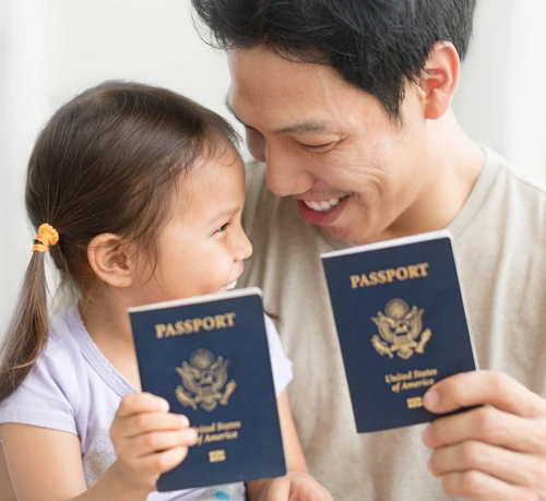 A man and a little girl joyfully hold up two passports, celebrating their successful passport application together.